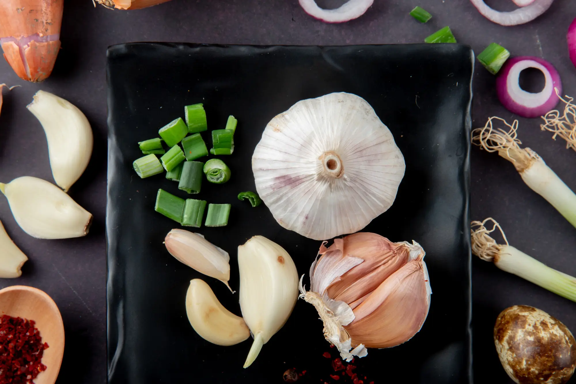 close-up-view-vegetables-as-garlic-bulb-cloves-cut-scallion-egg-onion-slice-maroon-background