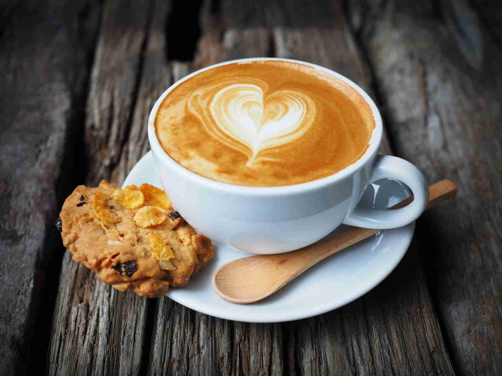 Cup of coffee with heart design drawn in foam on a wooden table.